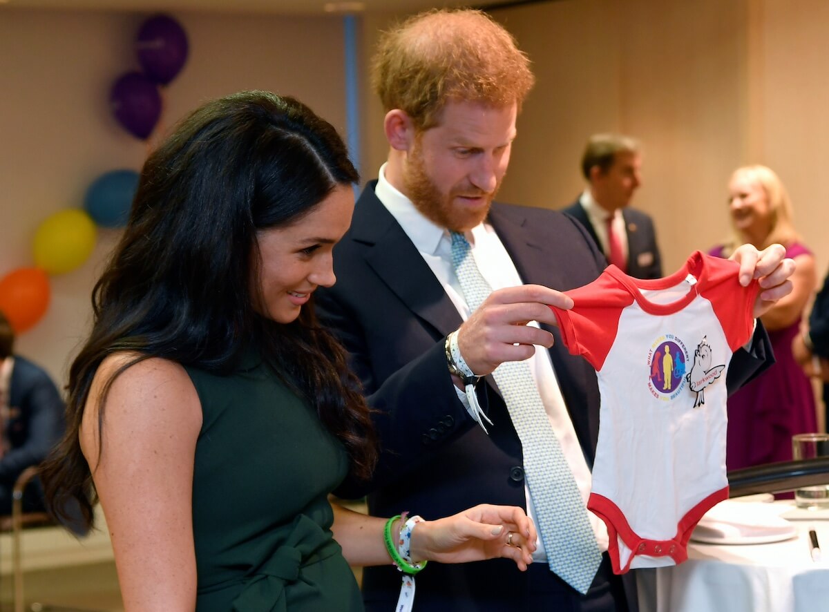 Prince Harry and Meghan Markle holding a onesie