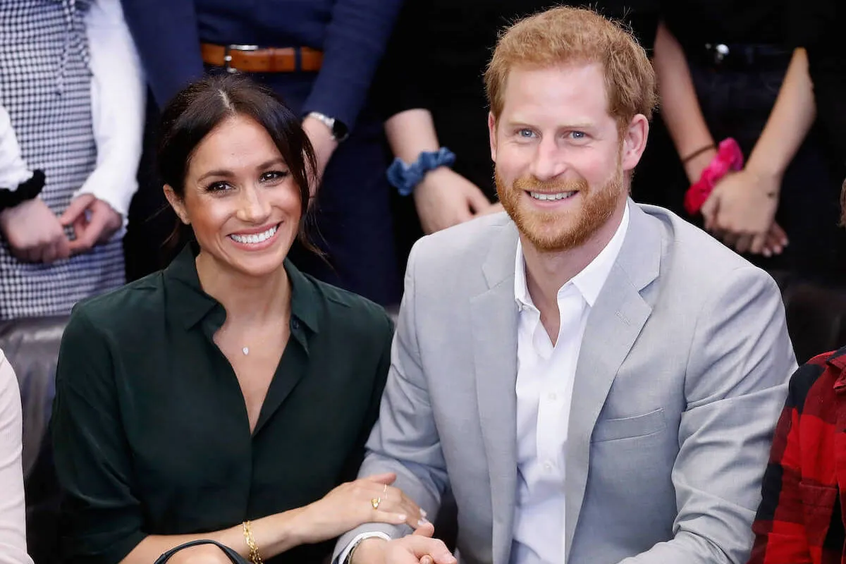 Prince Harry and Meghan Markle, who are 'moving on' from royal family drama at different speeds, smile as they sit next to each other in 2018