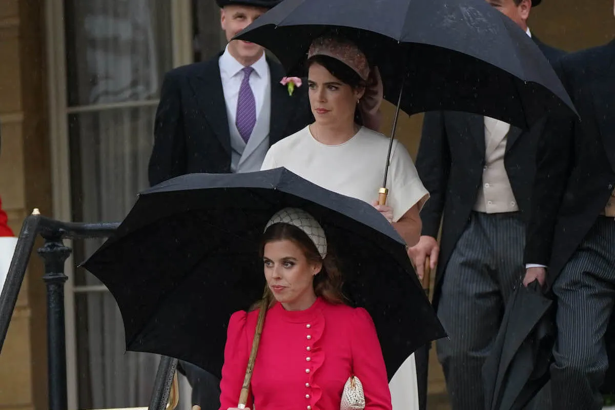 Princess Beatrice and Princess Eugenie, who aren't reportedly talking to Prince Harry, at a Buckingham Palace garden party holding umbrellas