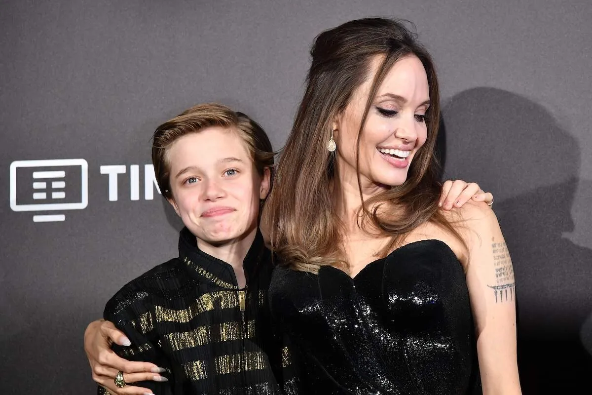 Wearing a black dress, Angelina Jolie poses with her daughter Shiloh Nouvel Jolie-Pitt, who's wearing a gold and black jacket