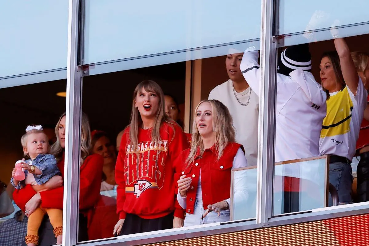 Taylor Swift and Brittany Mahomes wears red and stand in a box at a Chiefs game.