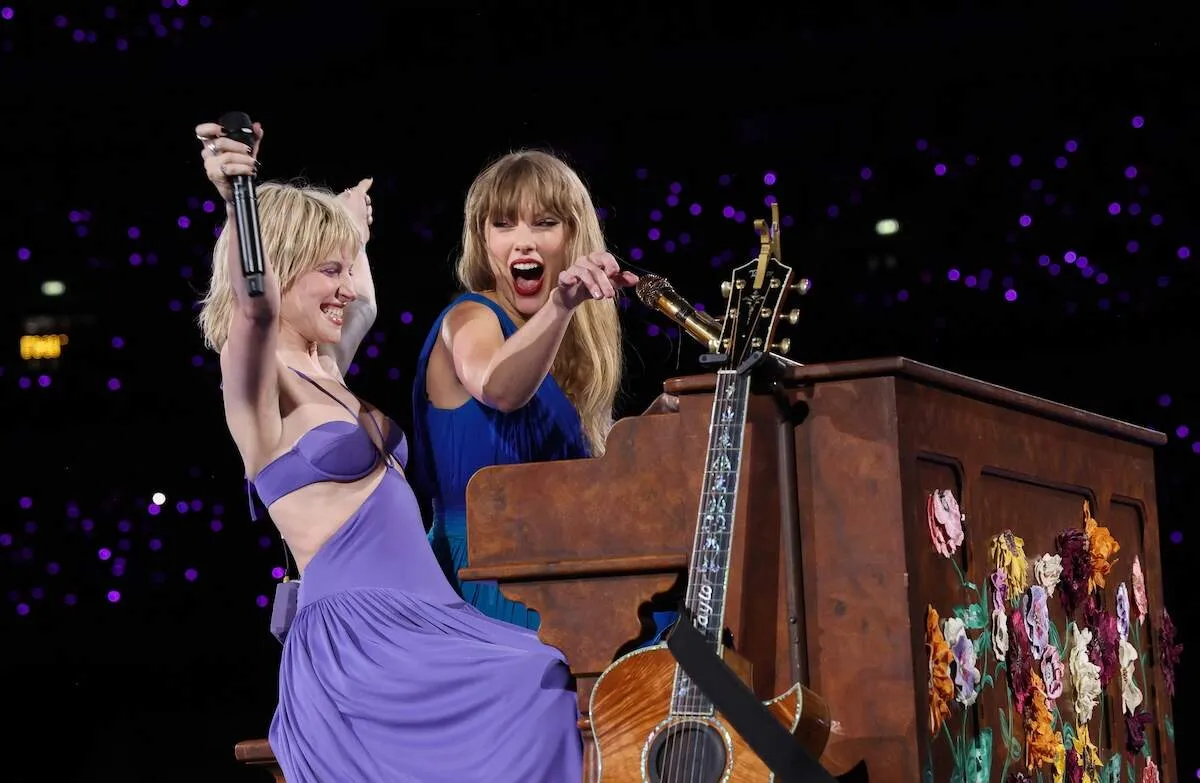 Wearing a blue gown, Taylor Swift and Hayley Williams play piano onstage in London
