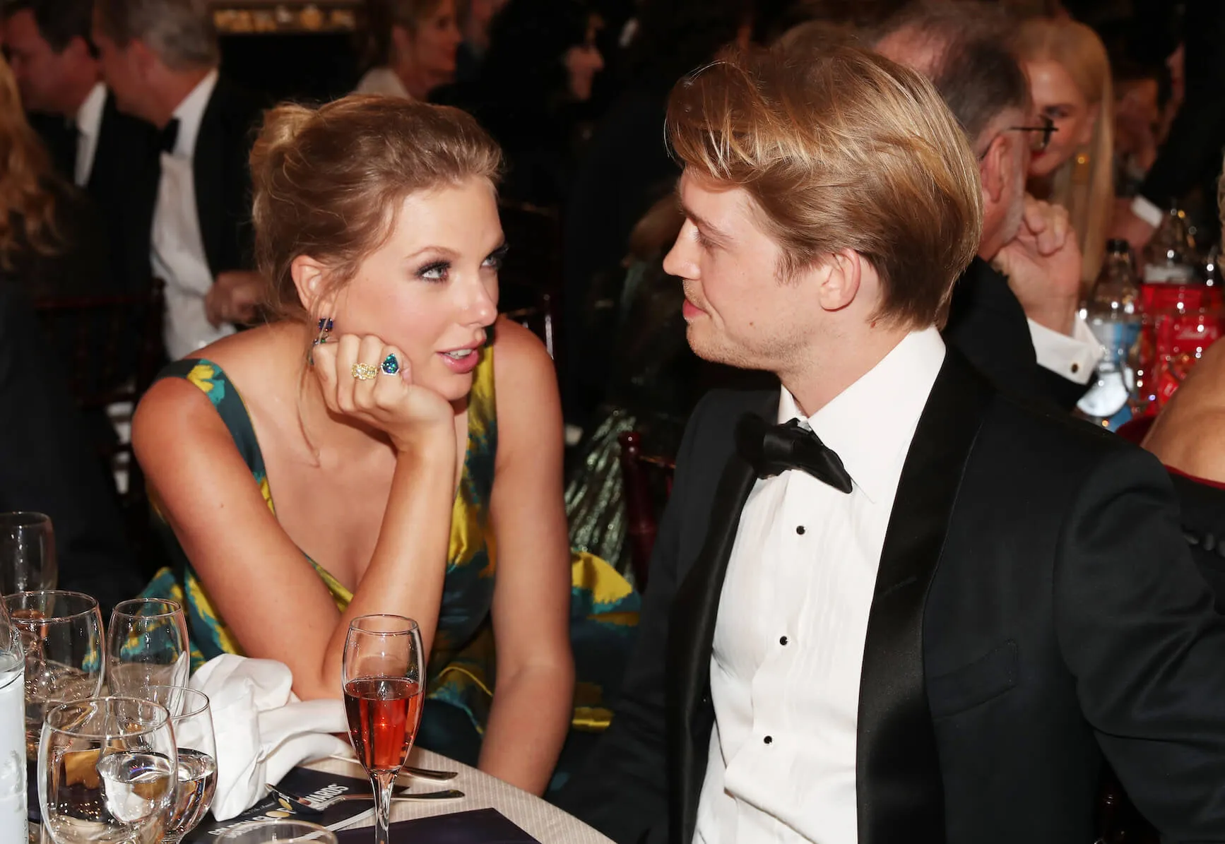 Taylor Swift with her chin in her hand looking at Joe Alwyn while sitting at a table at the 77th Annual Golden Globes