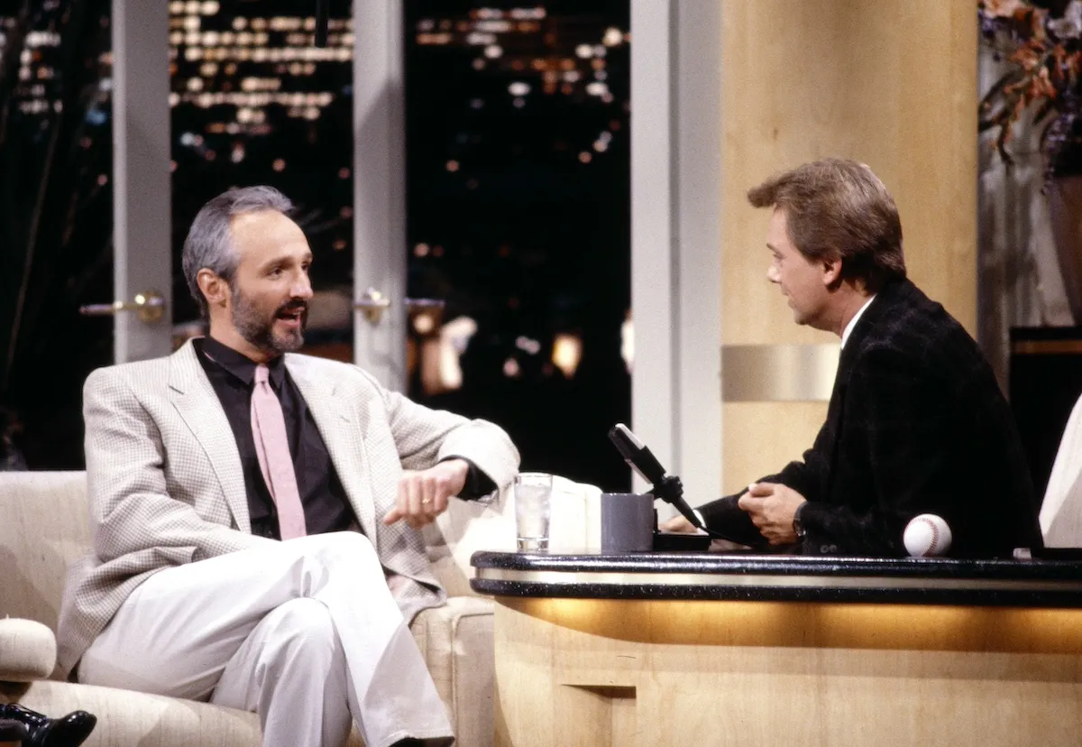 Pat Sajak, sitting behind a desk, interviews Michael Gross on 'The Pat Sajak Show'