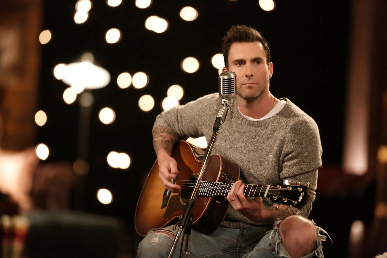 'The Voice' star Adam Levine sitting on a stool while playing guitar 