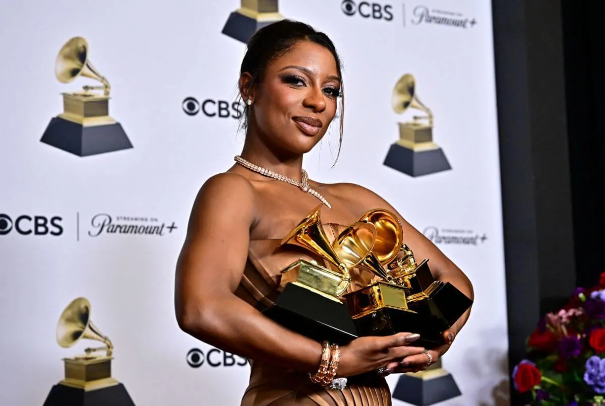 Victoria Monet holds three Grammy awards. She wears a necklace.