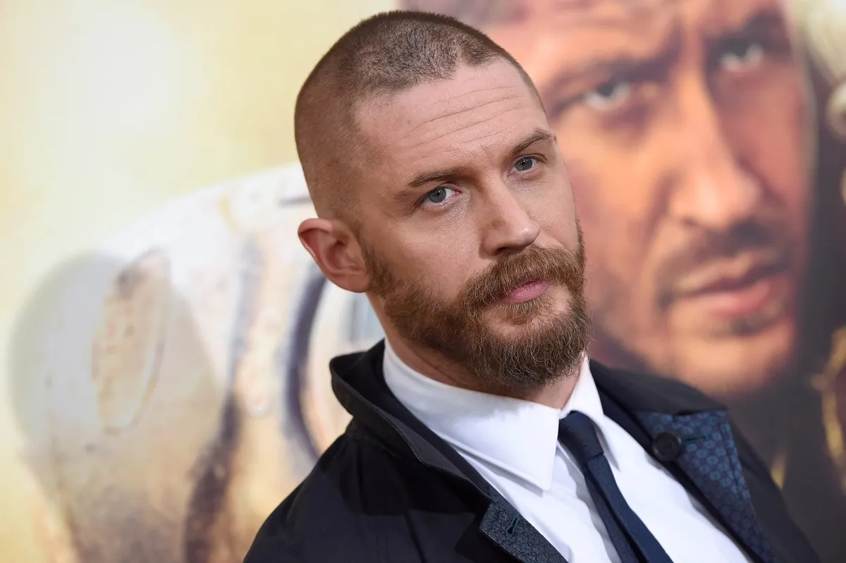 Tom Hardy posing at the 'Max Max Fury Road' premiere wearing a black trench troat.