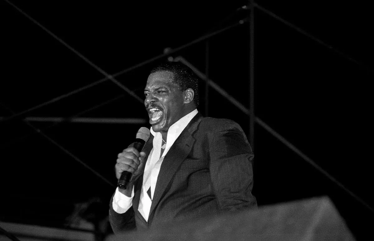 A black and white picture of Alexander O'Neal singing into a microphone while wearing a suit.