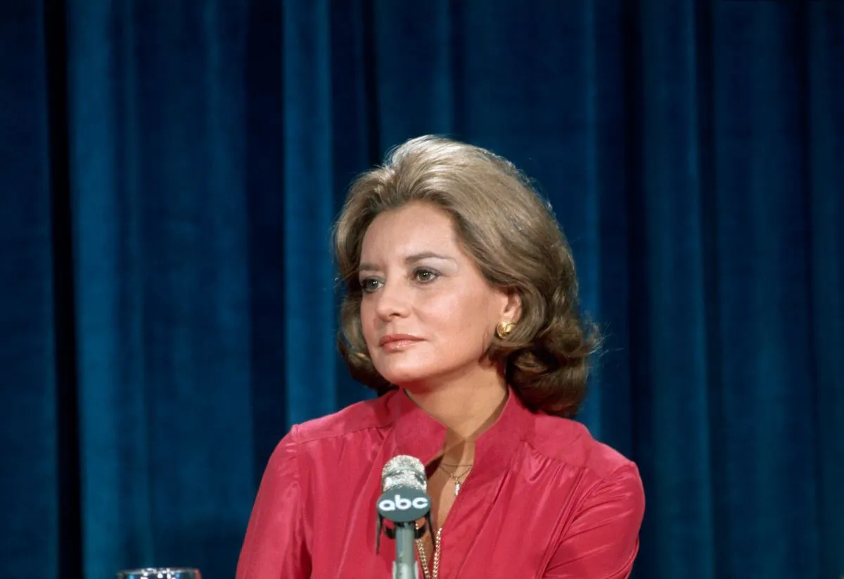 Barbara Walters wears a red shirt and sits in front of a microphone.