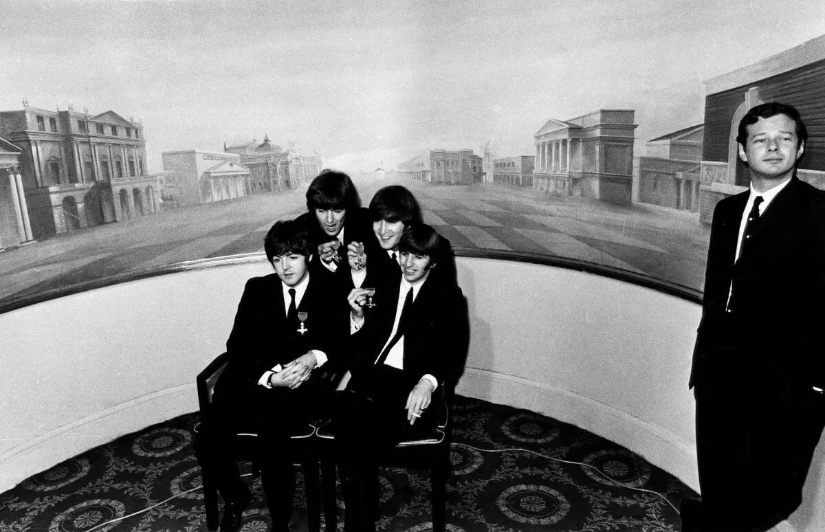 A black and white picture of The Beatles posing with their MBEs. Brian Epstein stands to the side.