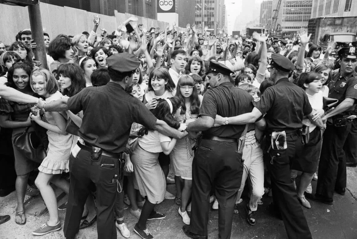 A black and white picture of police officers trying to hold back a crowd of The Beatles' fans.