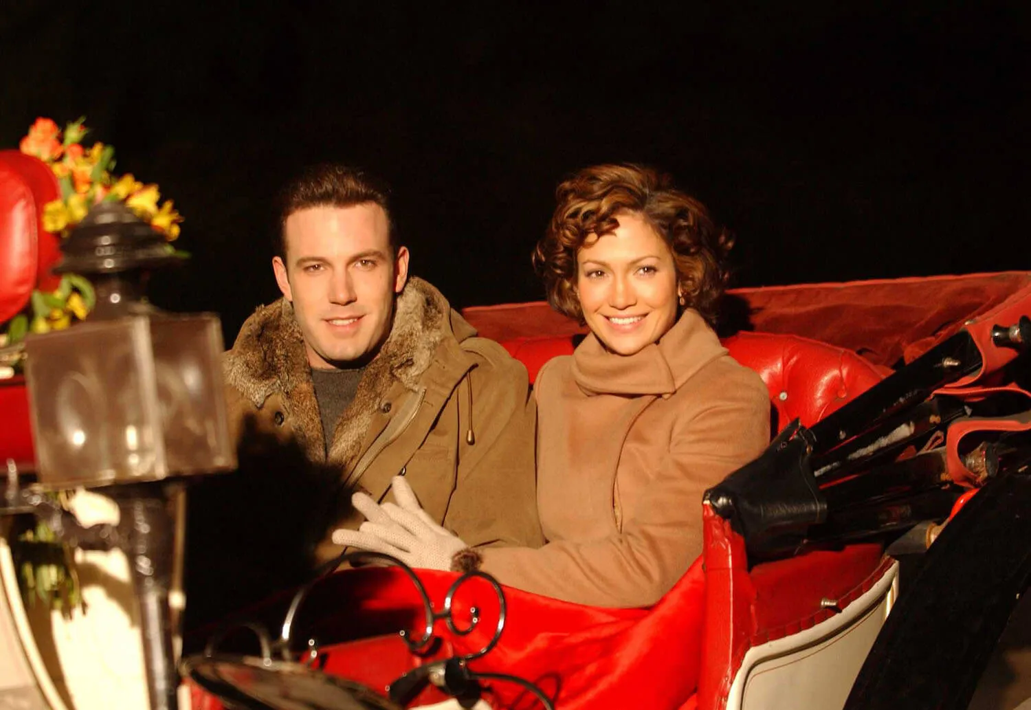 Ben Affleck and Jennifer Lopez smiling while riding a horse carriage in 2002
