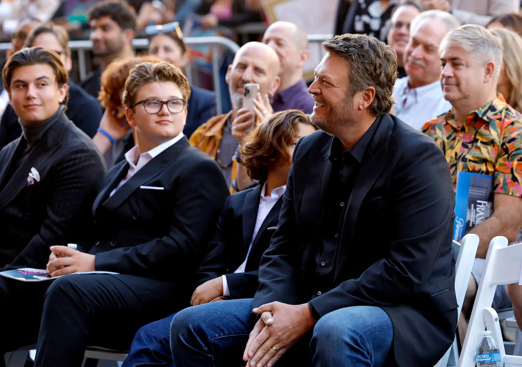 Kingston Rossdale, Zuma Rossdale, Apollo Rossdale, and Blake Shelton sitting next to each other and smiling at the Hollywood Walk of Fame Star Ceremony Honoring Gwen Stefani in 2023