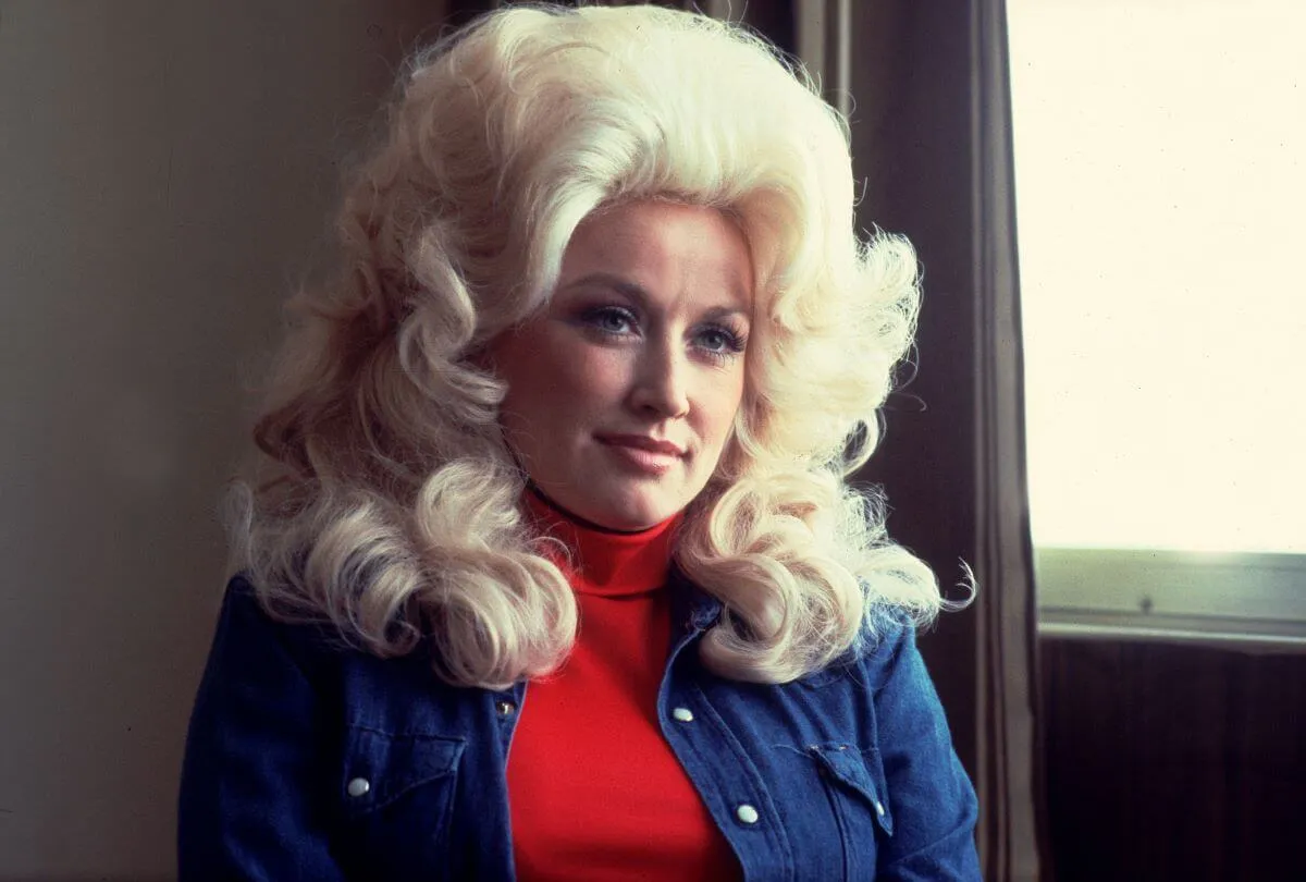 Dolly Parton wears a red turtleneck and a denim shirt.