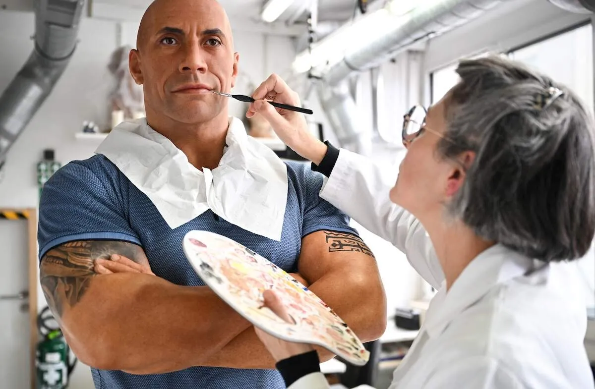 An adjusted wax figure of Dwayne Johnson is painted by a museum employee