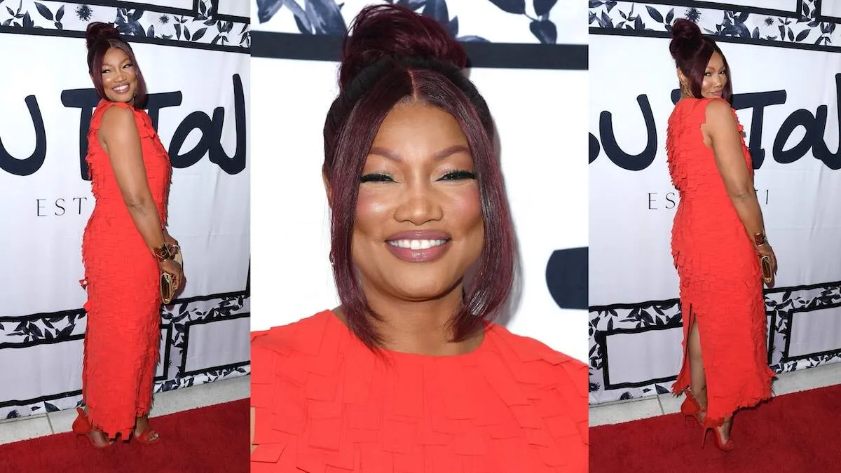 Wearing a red dress, Garcelle Beauvais smiles on the red carpet before Sutton Stracke's fashion show