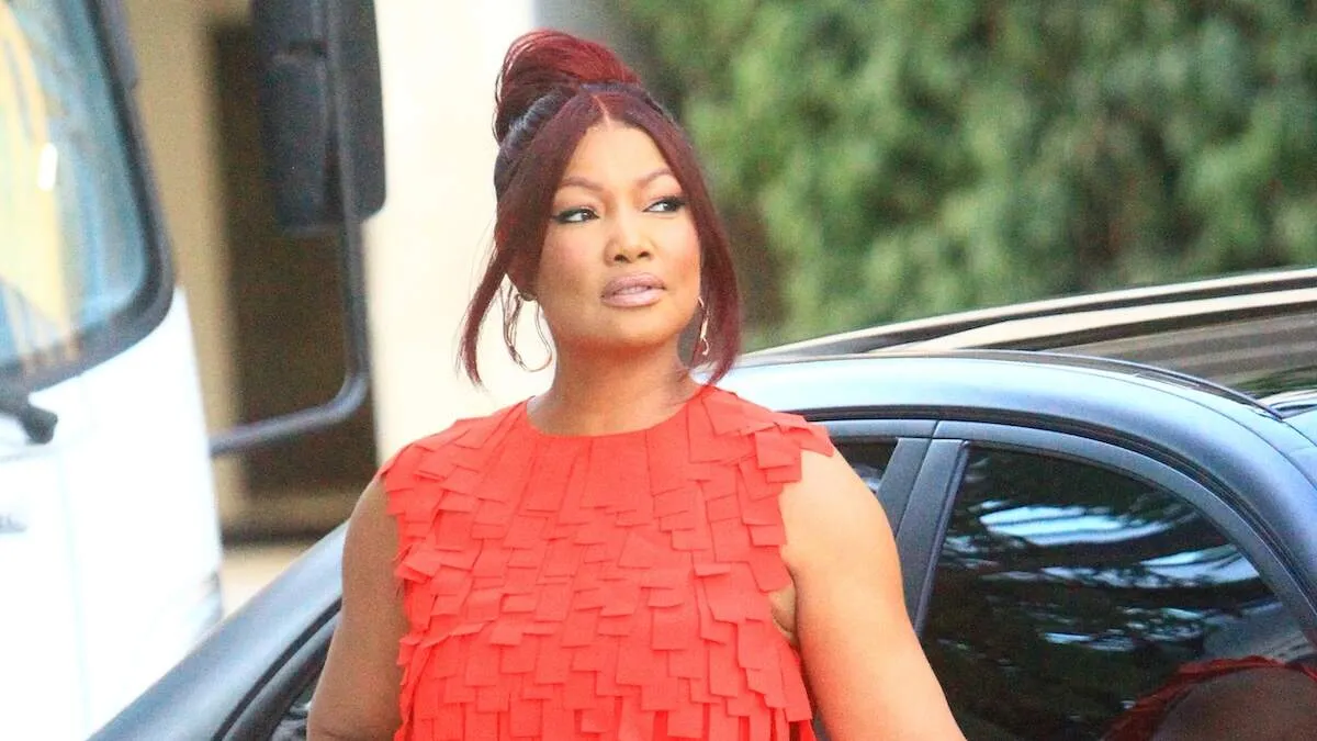 Real Housewives star Garcelle Beauvais stands next to a black car and poses in a red dress