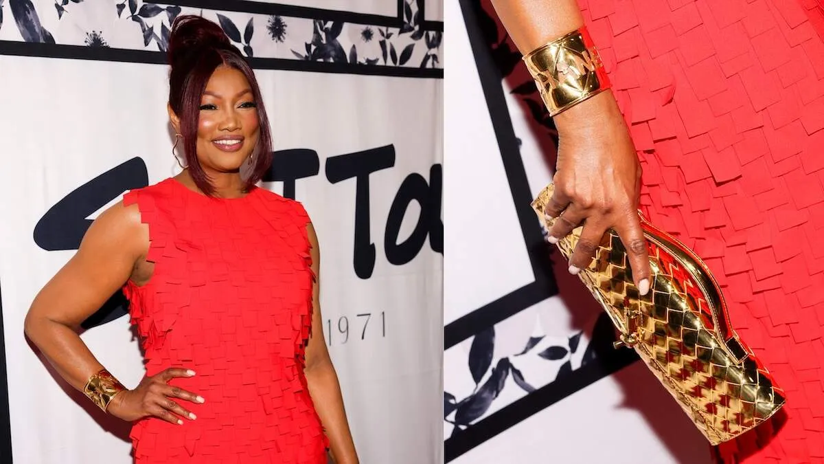 Wearing a red dress, Garcelle Beauvais smiles on the red carpet before Sutton Stracke's fashion show