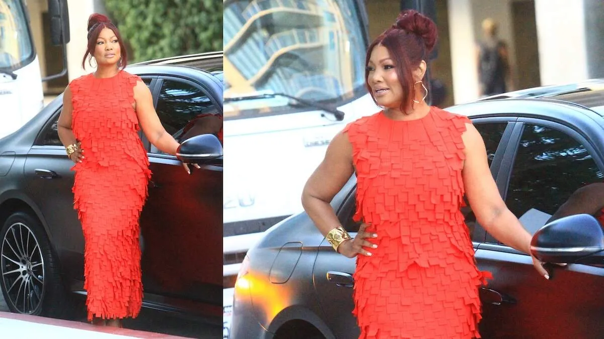 Real Housewives star Garcelle Beauvais stands next to a black car and poses in a red dress