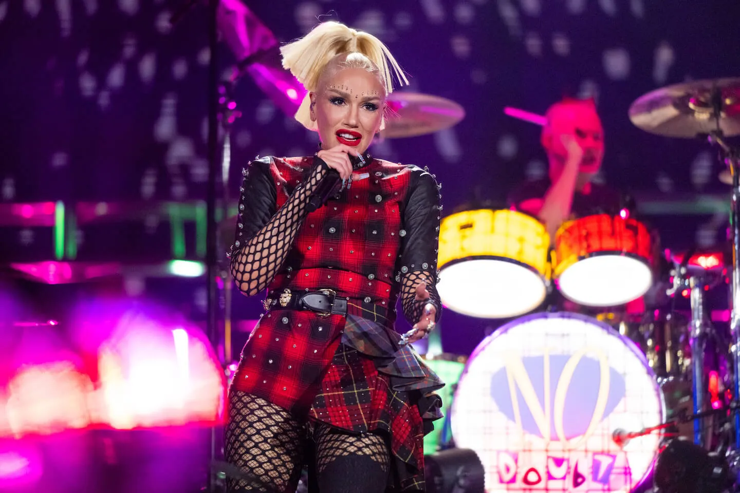 Gwen Stefani on stage in a red and black plaid outfit with the No Doubt drummer in the background at Coachella in April 2024