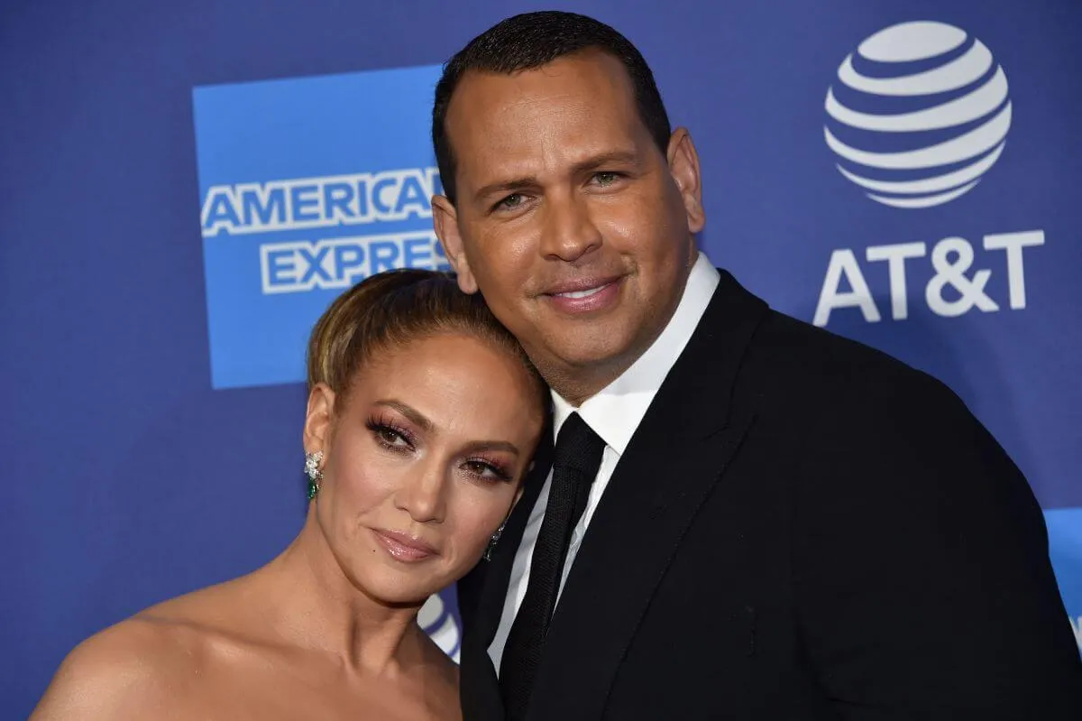 Jennifer Lopez leans on Alex Rodriguez's shoulder. They stand in front of a blue background.