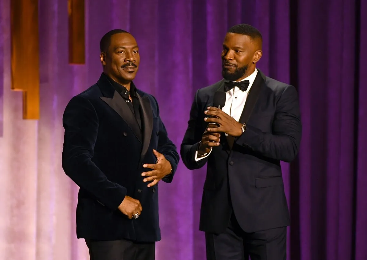 Eddie Murphy and Jamie Foxx speak onstage during the Academy Of Motion Picture Arts And Sciences' 11th Annual Governors Awards while wearing suits.