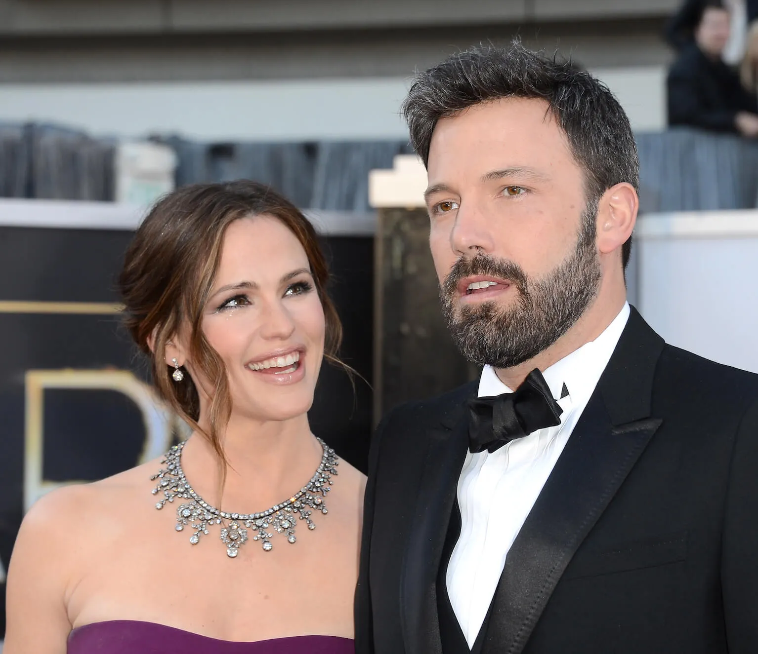 Jennifer Garner in a purple dress smiling and looking up at Ben Affleck as he talks at the Academy Awards in 2013