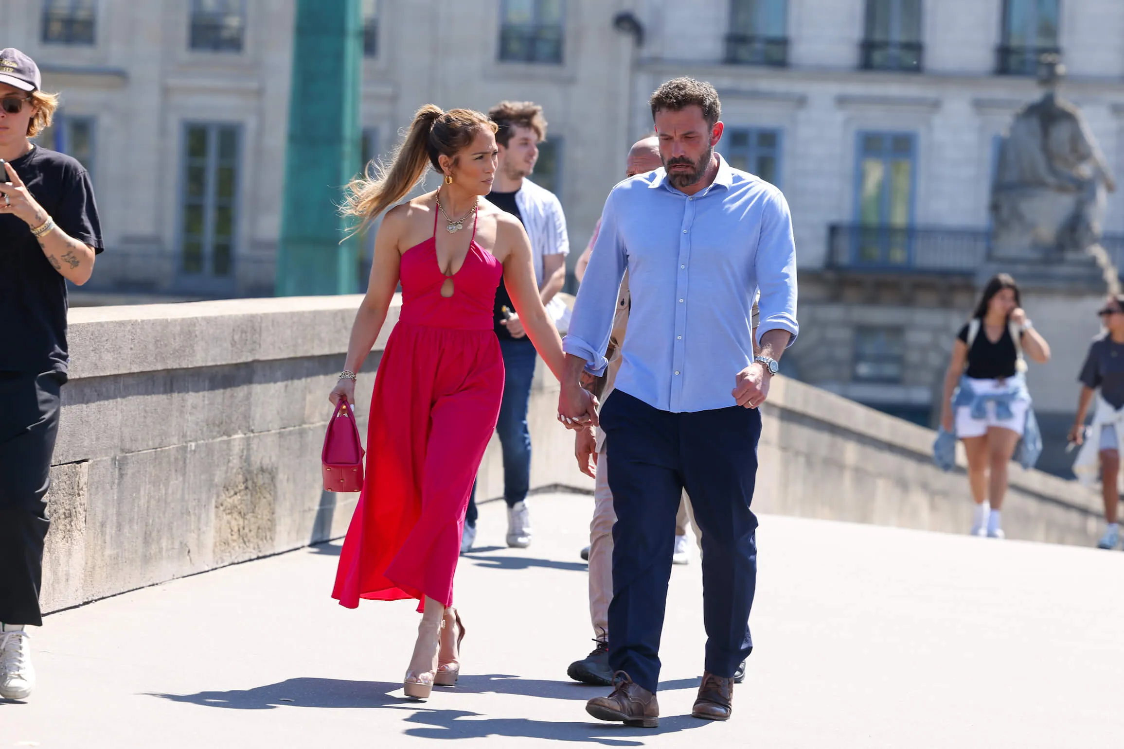 Jennifer Lopez in a bright red dress and Ben Affleck in a blue button-down shirt walking in Paris in 2022