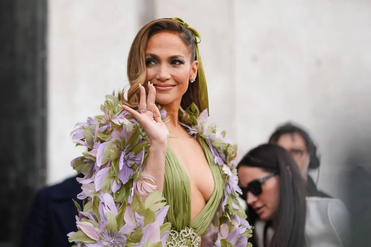 Kamala Harris wears a green and purple dress with floral sleeves. She wears a green ribbon in her hair and waves.