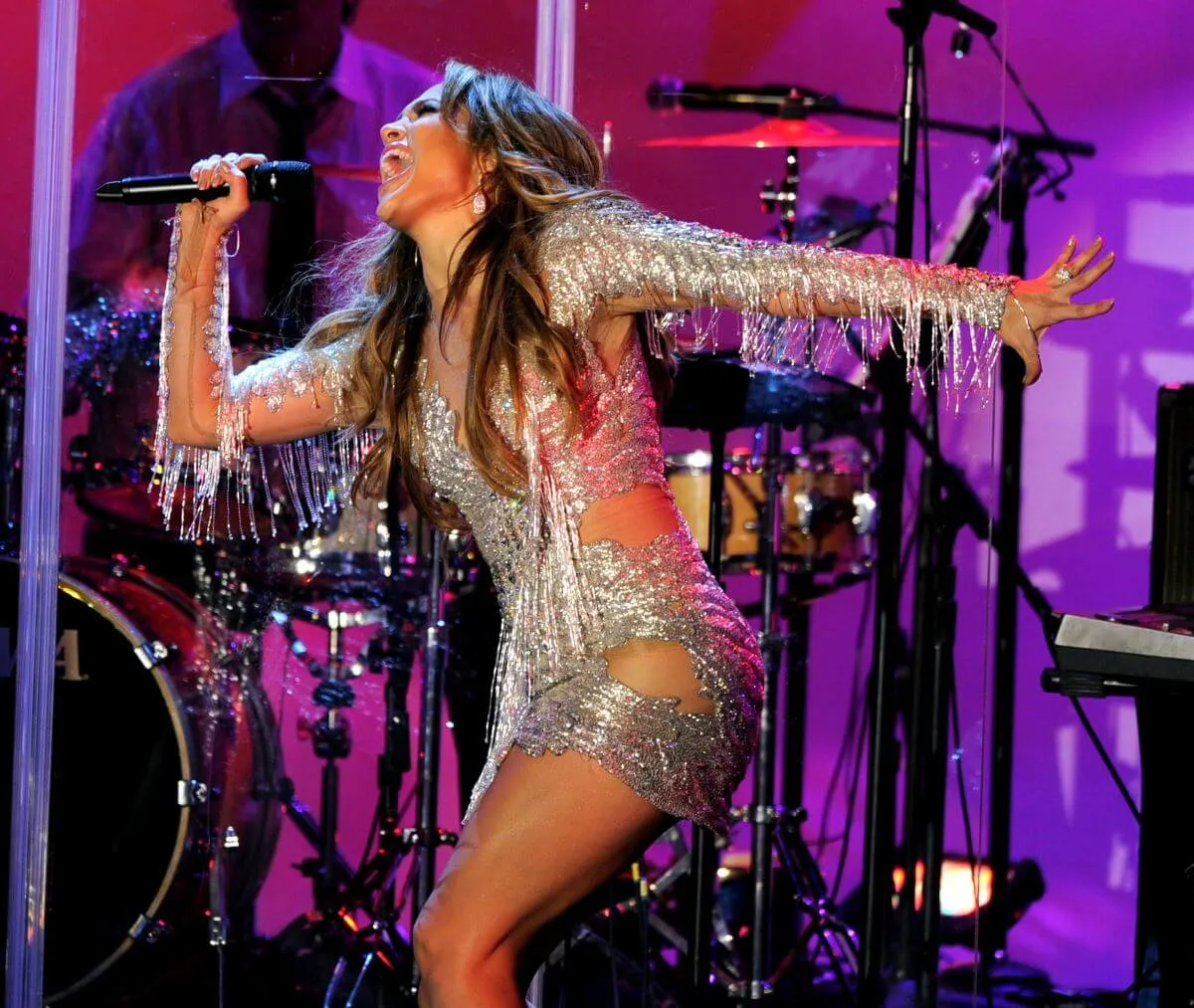 Jennifer Lopez wears a silver dress and sings into a microphone.