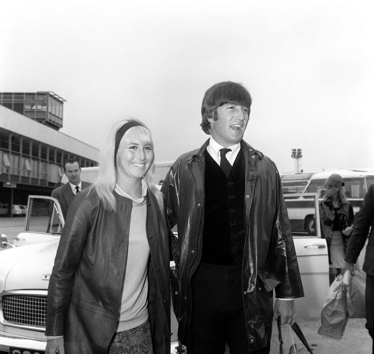 A black and white picture of Cynthia and John Lennon walking outside at an airport.