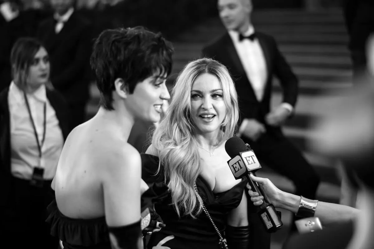 A black and white picture of Madonna looking at Katy Perry as she speaks into a microphone.
