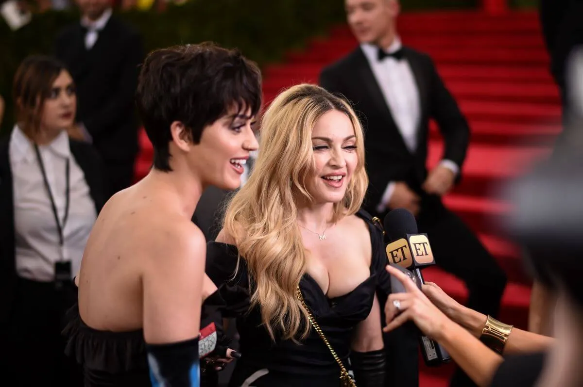 Katy Perry and Madonna talk into the same microphone while on the red carpeted steps of the Met Gala.