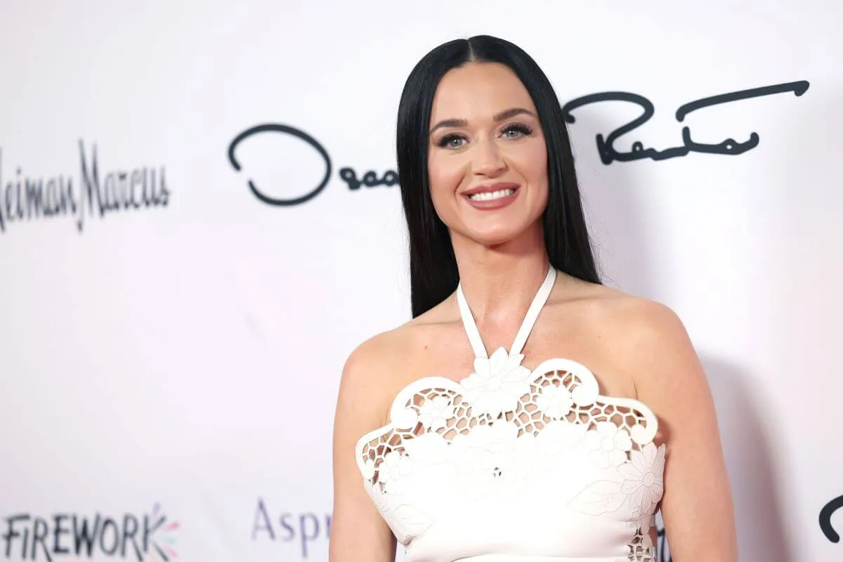 Katy Perry wears a white, lacy halter top and stands in front of a white background.