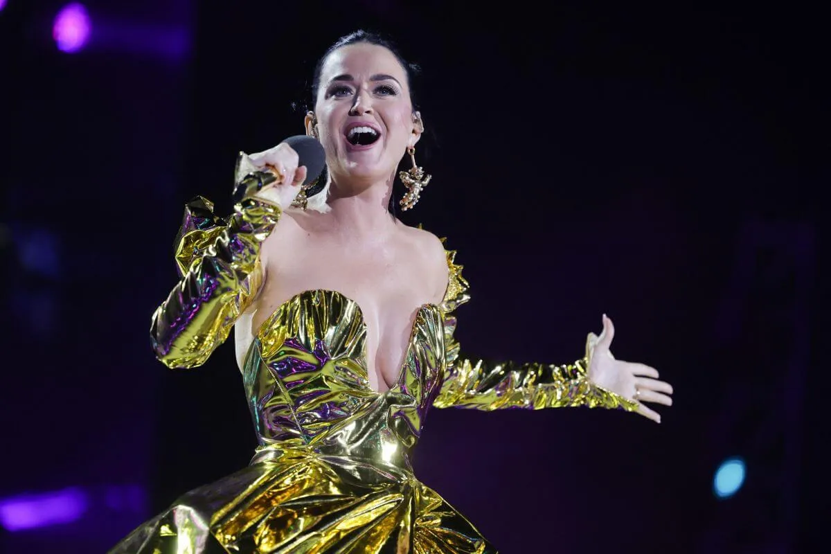 Katy Perry wears a metallic golden dress and speaks into a microphone.
