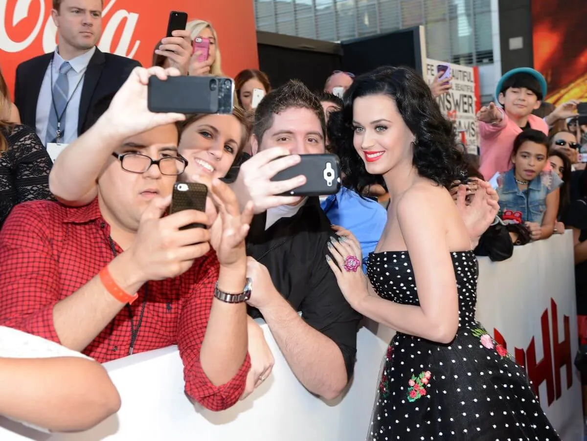 Katy Perry wears a black polka dot dress and poses for photos with a group of fans.