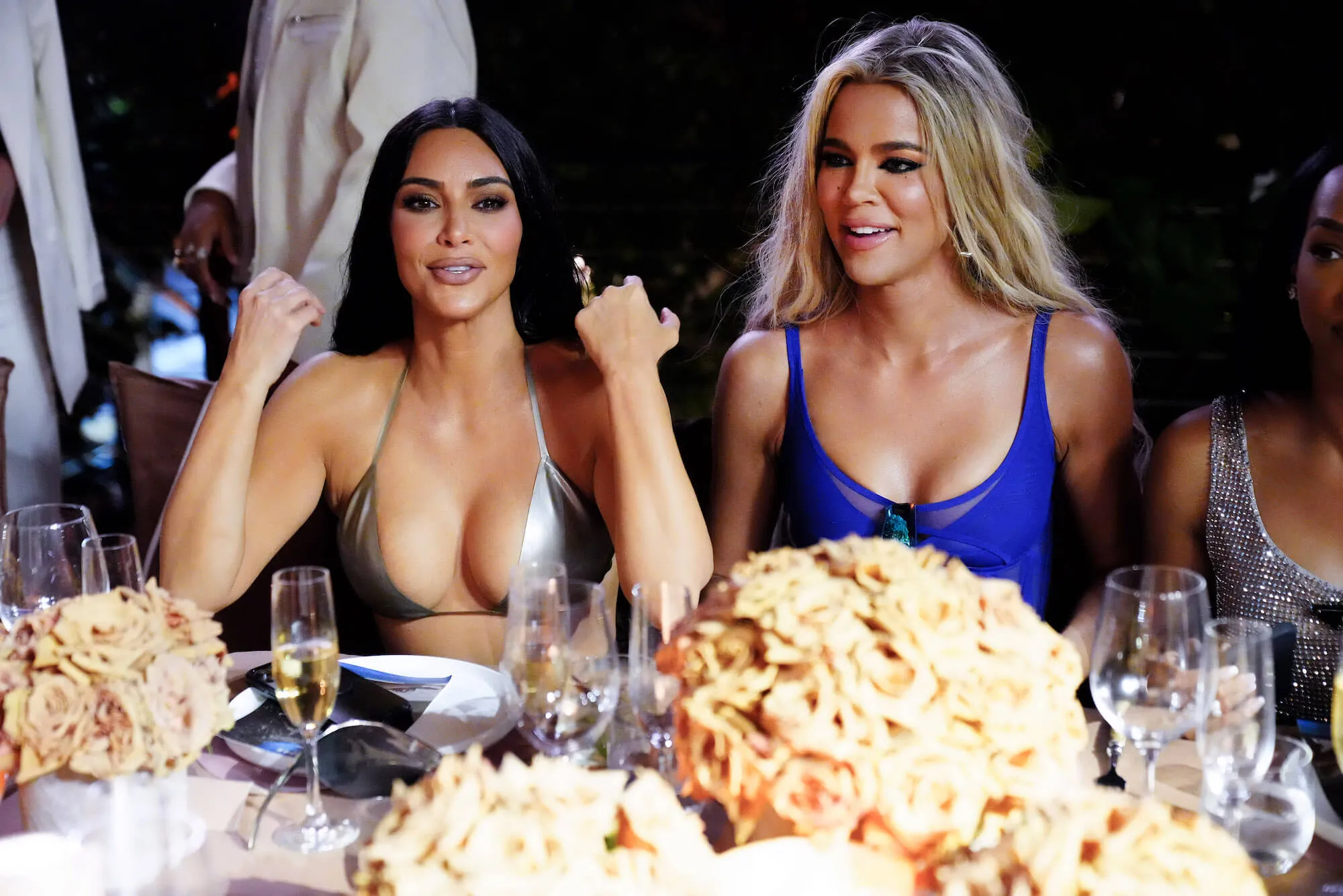 Kim and Khloé Kardashian smiling at a table together at the SKIMS SWIM Miami pop-up dinner at SWAN on March 19, 2022, in Miami, Florida