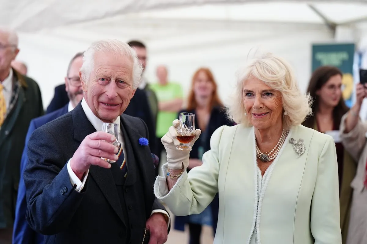 King Charles and Queen Camilla raise glasses in a toast. 