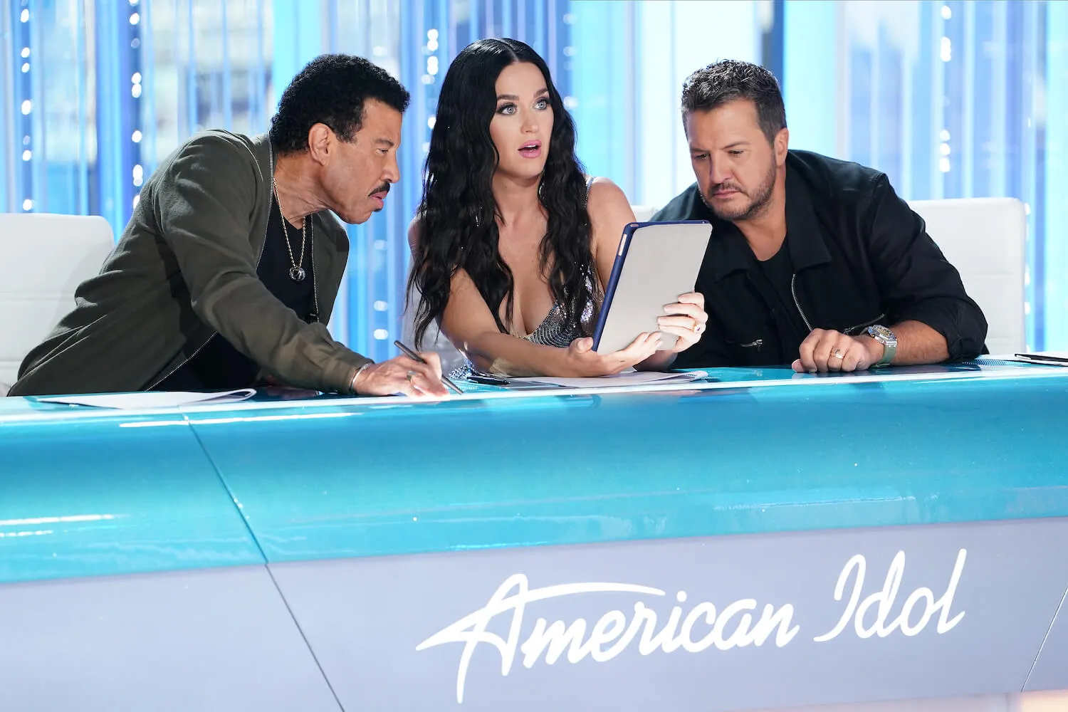 Lionel Richie, Katy Perry, and Luke Bryan looking at a piece of paper together on 'American Idol.' Perry looks shocked.