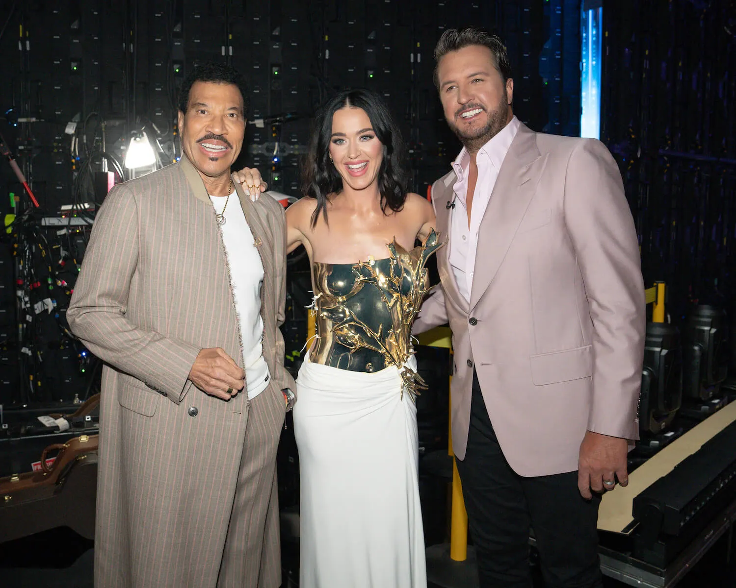 Lionel Richie, Katy Perry, and Luke Bryan from 'American Idol' with their arms around each other and smiling against a dark background