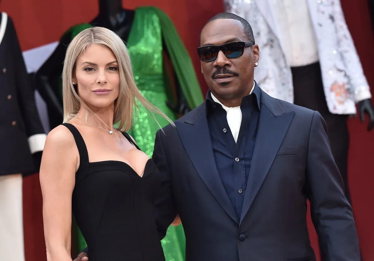 Wearing a black dress and navy suit, Paige Butcher and Eddie Murphy pose together on a red carpet after getting engaged in 2019