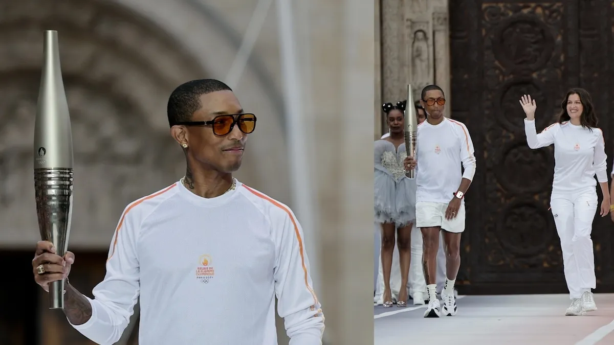 Wearing a white long sleeve and white shorts, Pharrell carries the Olympic torch at the opening ceremony relay