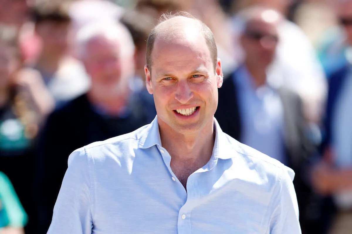 Prince William, who got compared to Princess Diana for taking Princess Charlotte and Prince George to Taylor Swift's concert, smiles wearing a blue shirt