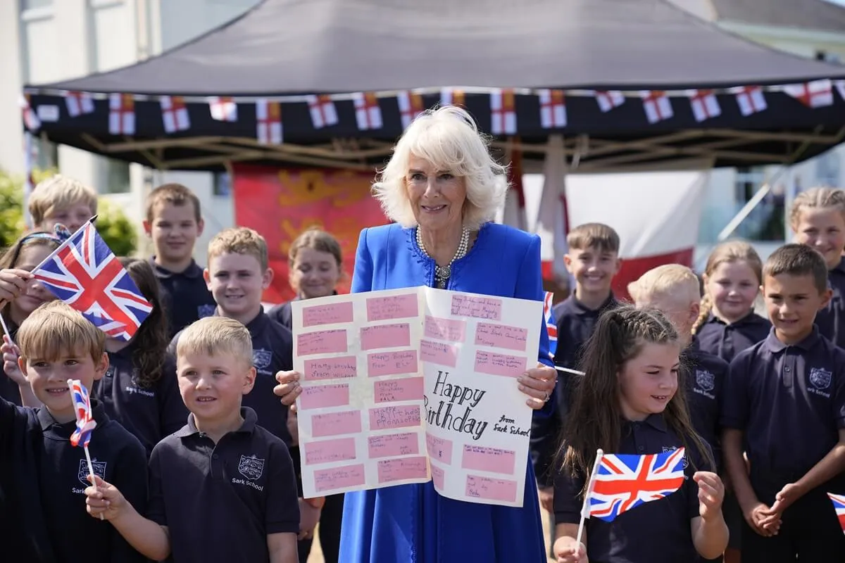 Queen Camilla poses with local school children holding a birthday card during an official visit to Guernsey