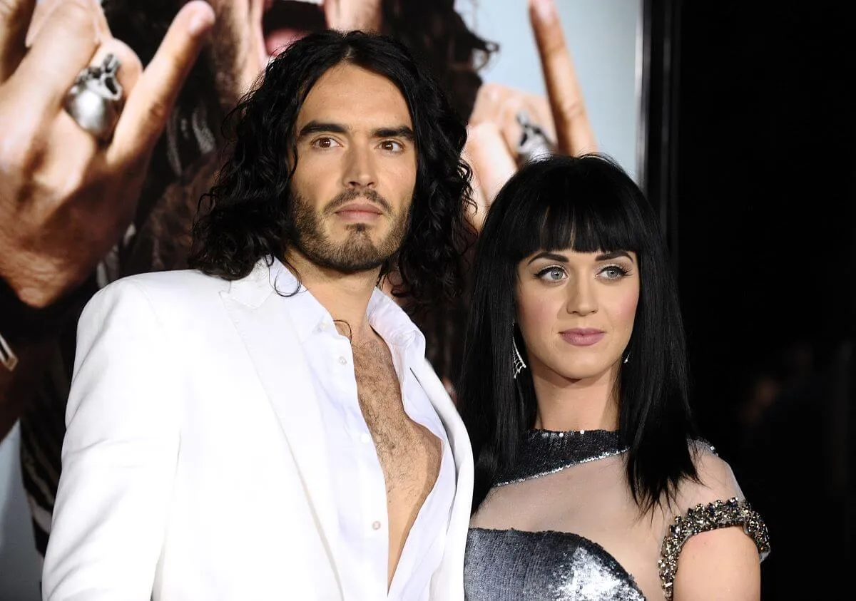 Russell Brand wears a white shirt and stands next to Katy Perry, who wears a silver dress.