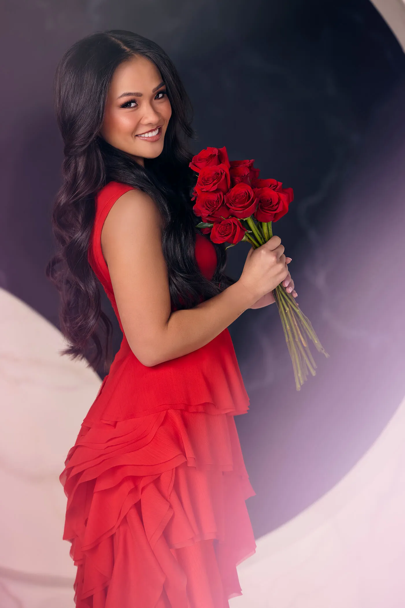'The Bachelorette' Season 21 star Jenn Tran in a red dress holding red roses and looking over her shoulder while smiling