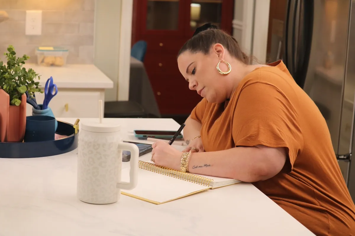 Whitney Way Thore sitting at a table and writing in a notebook in 'My Big Fat Fabulous Life'
