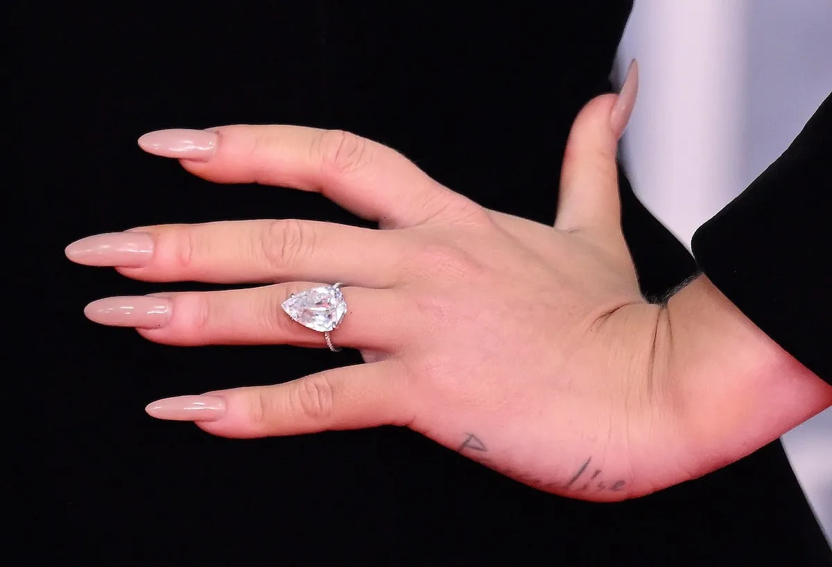 Wearing a black gown, Adele wears a pear-shaped ring on her left hand's ring finger at the 2022 Brit Awards