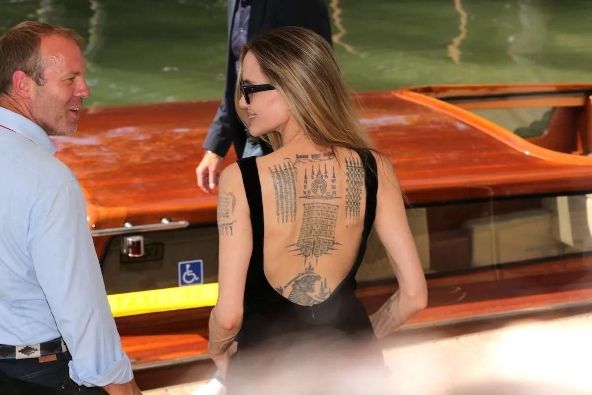 Wearing a black dress, Angelina Jolie stands alongside the river in Venice and offers a closeup of her back tattoos