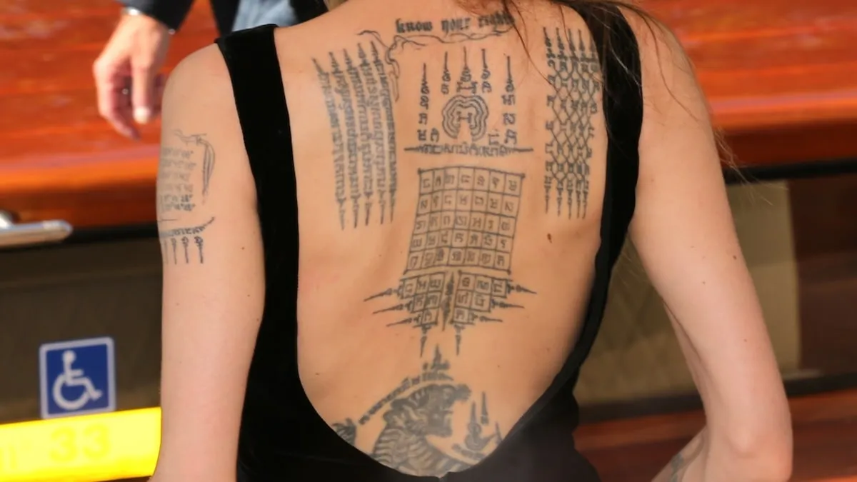 Wearing a black dress, Angelina Jolie stands alongside the river in Venice and offers a closeup of her back tattoos